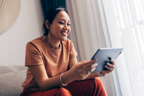 Smiling woman sitting indoors and using a digital tablet, possibly engaging with an online course or business resource