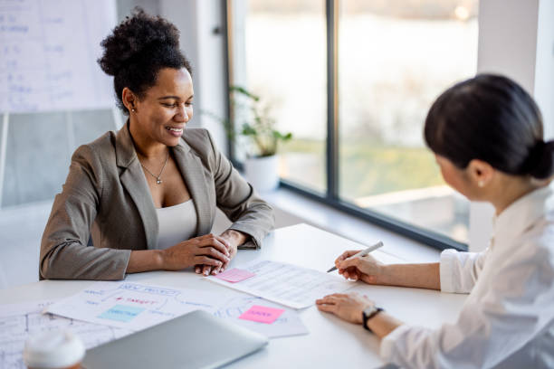 Two women in a bright office setting discussing business plans and documents during a collaborative meeting.
