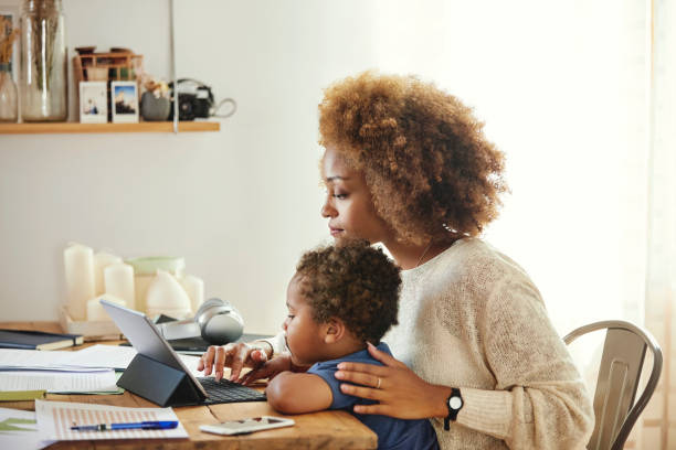 Woman working on a laptop at home with a young child on her lap.