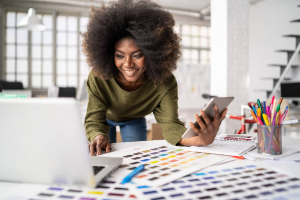 Woman smiling while working at a desk with color swatches and a smartphone.