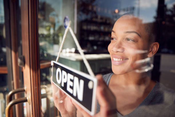 Smiling business owner hanging an 'Open' sign on the door of their storefront, ready to welcome customers.