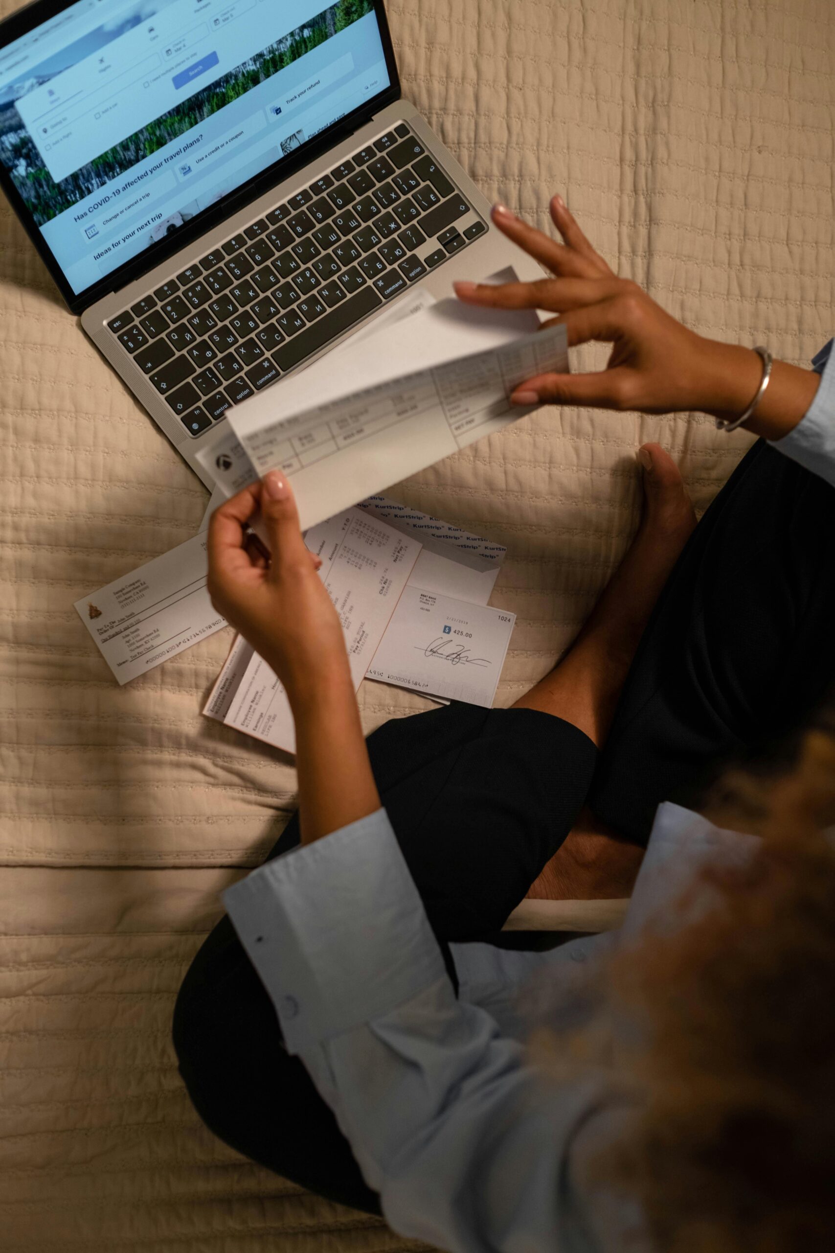 Person sitting with a laptop and reviewing financial documents and checks, managing bills or bookkeeping from home.