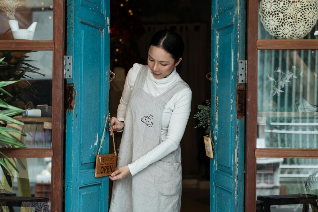 Small business owner opening a storefront door and hanging an 'Open' sign, preparing to welcome customers.