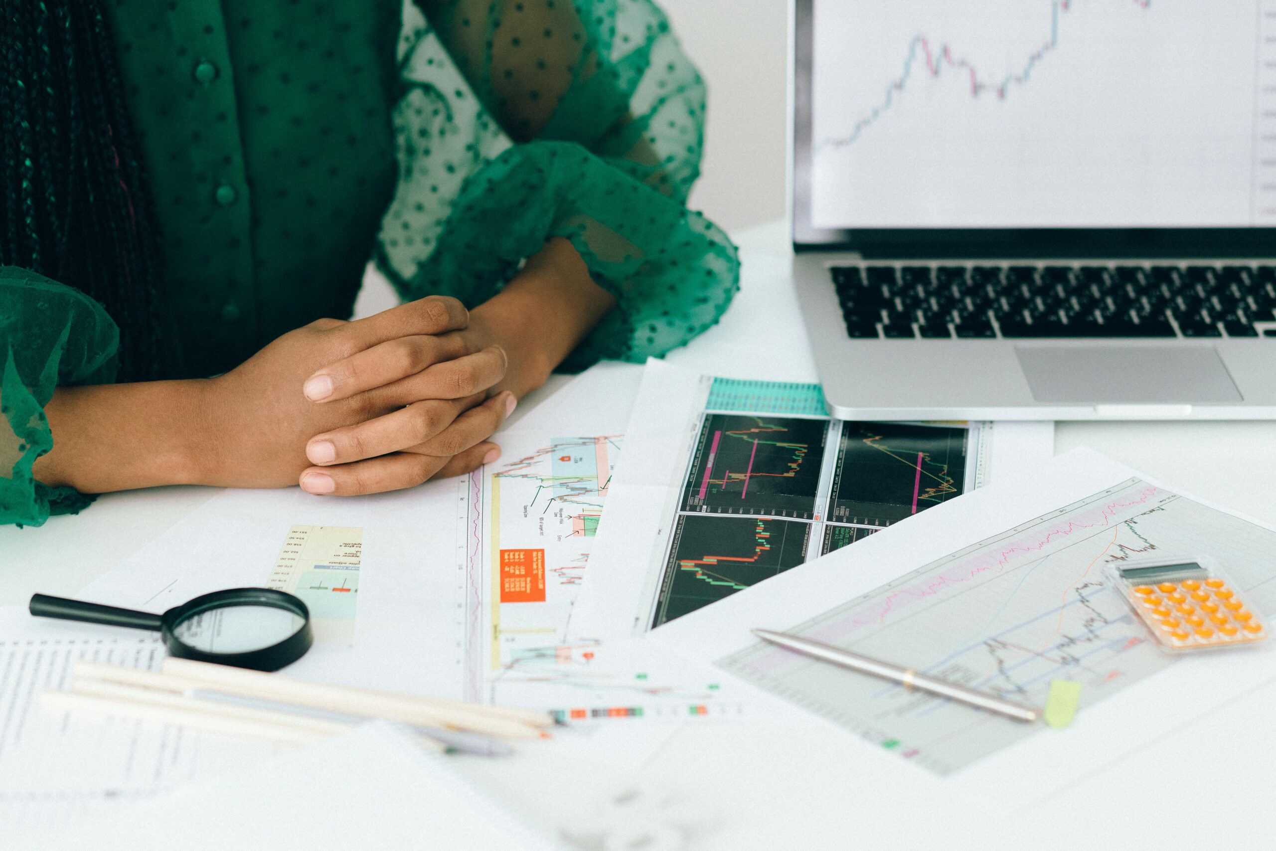 Person sitting at a desk with financial charts, documents, and a laptop, reviewing small business funding or investment options