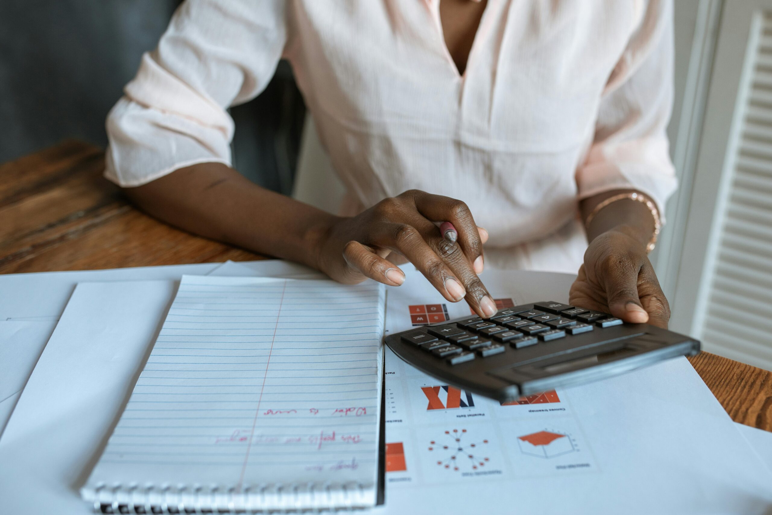 Person using a calculator and reviewing financial documents at a desk, with a notebook open for notes.