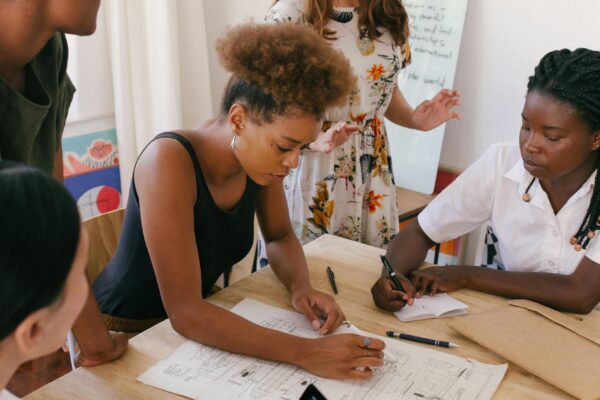 A diverse group of women entrepreneurs gathered around a table, reviewing blueprints and discussing business plans in a collaborative workspace.