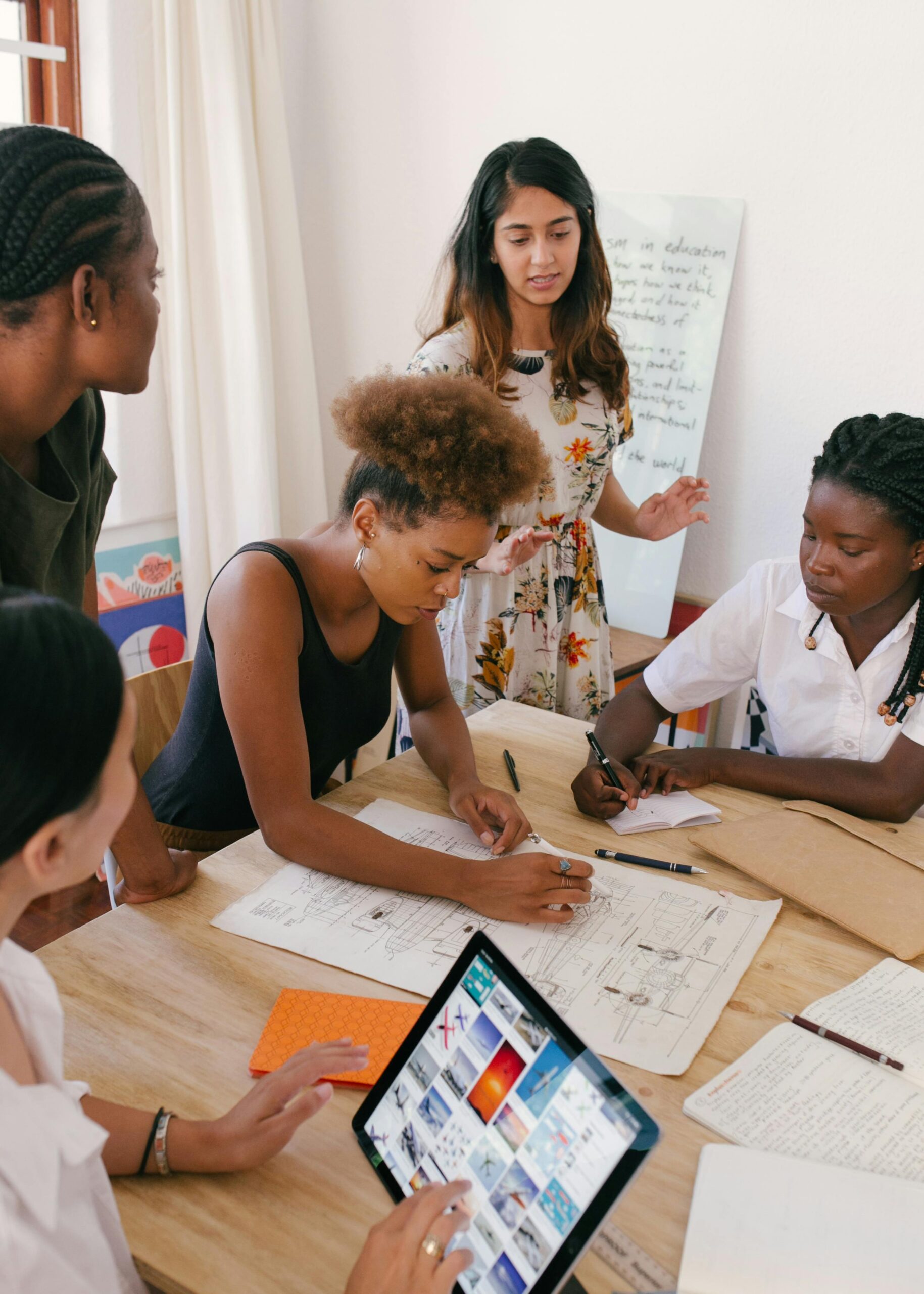 A diverse group of women entrepreneurs gathered around a table, reviewing blueprints and discussing business plans in a collaborative workspace.