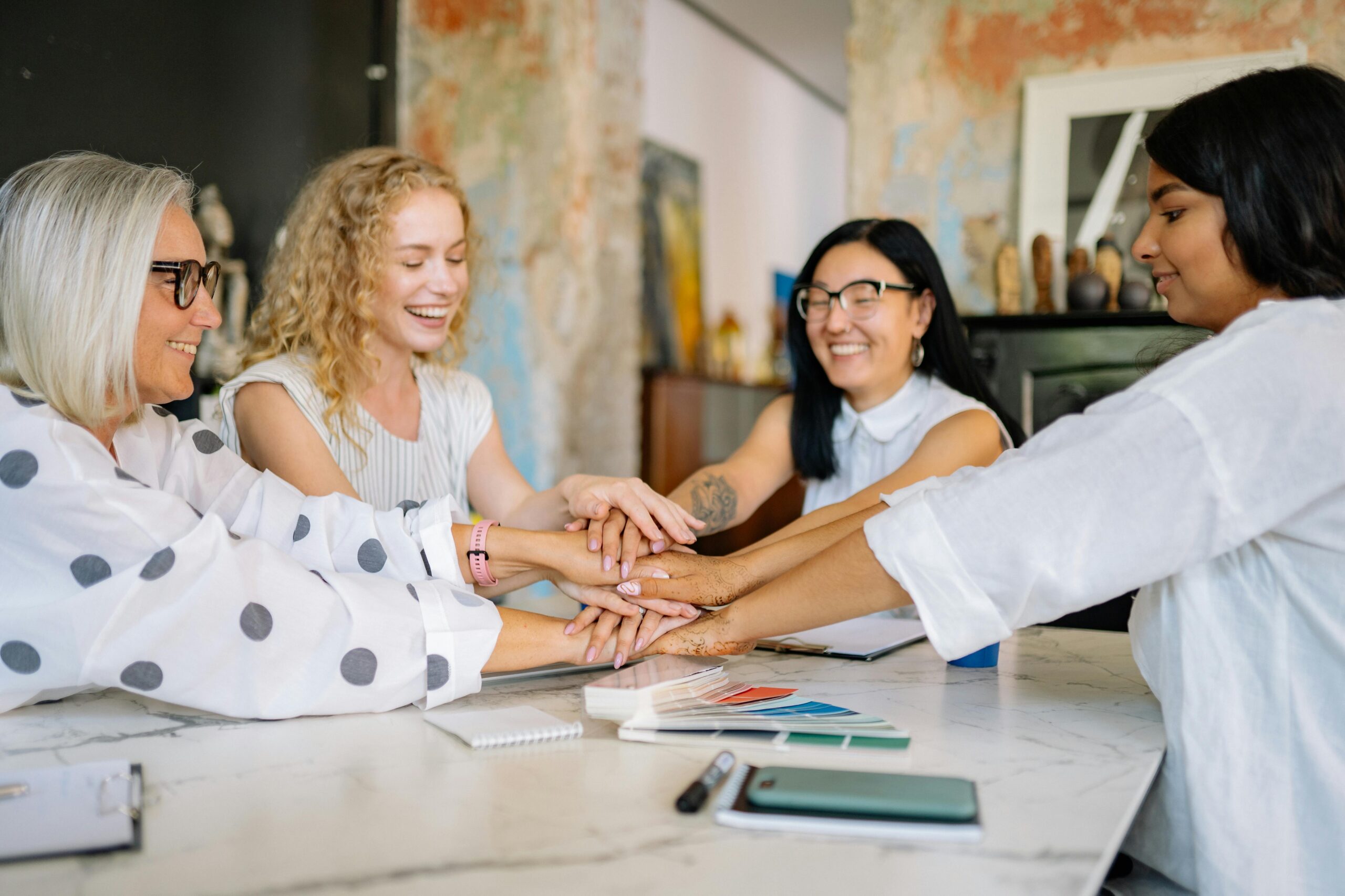 Group of women entrepreneurs smiling and stacking hands in a show of unity and support during a team meeting.